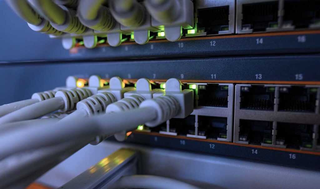 EDV- Service Bild. Der Hintereteil eines Netzwerkswitch (Patchpanel); Einige Netzwerkkabel führen heraus und die LDS Leuchten